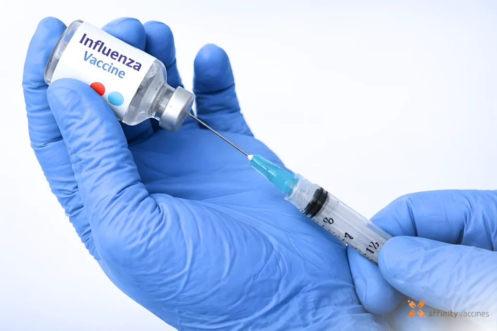 Gloved hands drawing influenza vaccine from a vial into a syringe against a clean white background.